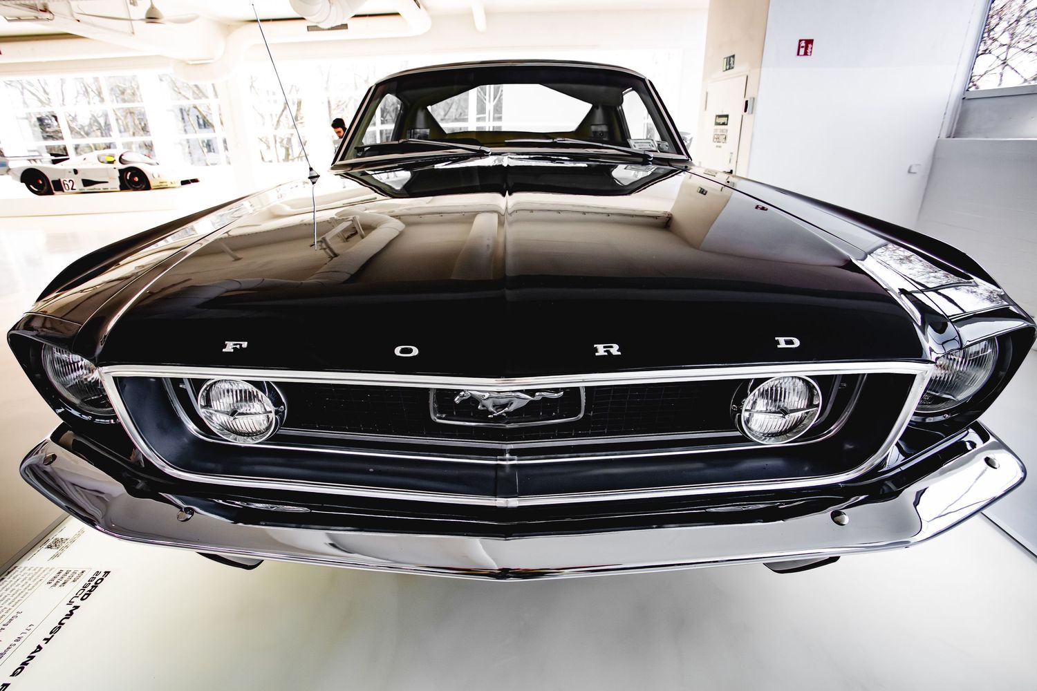 Front view of a classic black Ford Mustang with chrome grille in a bright white showroom.