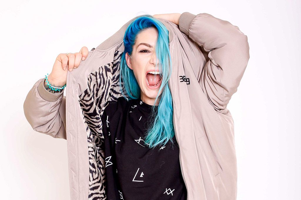 Young woman with blue hair laughing while wearing an oversized hoodie on white background.