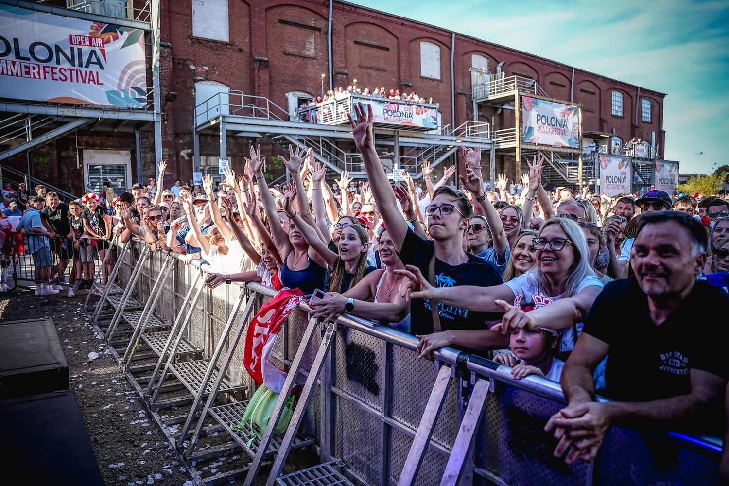 Excited crowd at Polonia Music Festival cheering behind barriers at an outdoor concert venue.