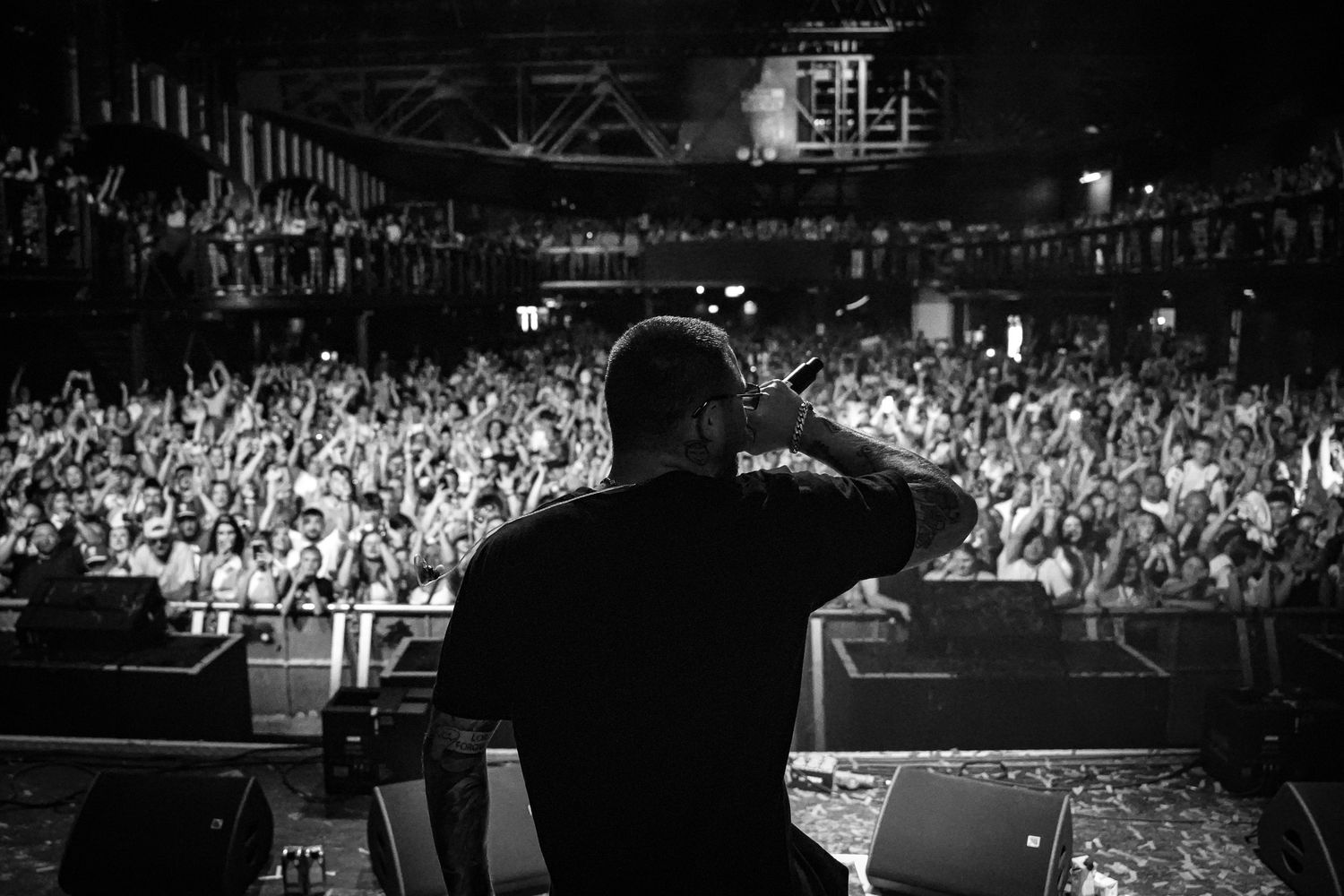 Black and white photo of a DJ performing on stage before a massive crowd at a packed concert venue.Polonia music festival