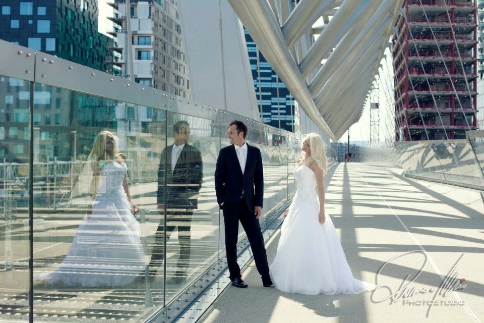 Bride and groom sharing a romantic moment on a modern glass bridge in an urban cityscape.