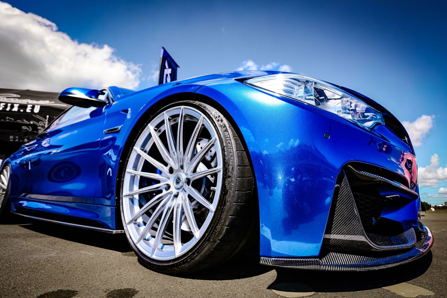 Close-up of a blue BMW sports car showcasing a large chrome alloy wheel and aggressive front bumper styling.