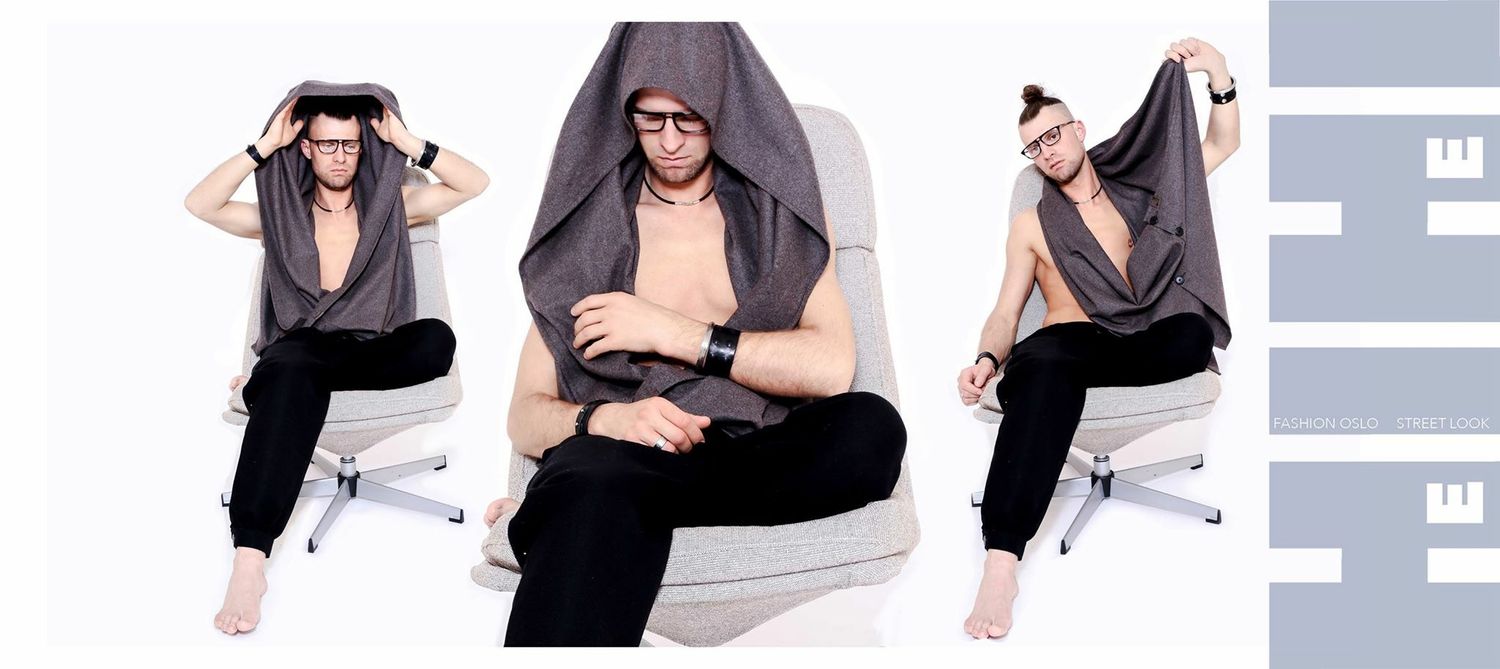 Man posing in grey hooded vest on white chair in fashion editorial spread.