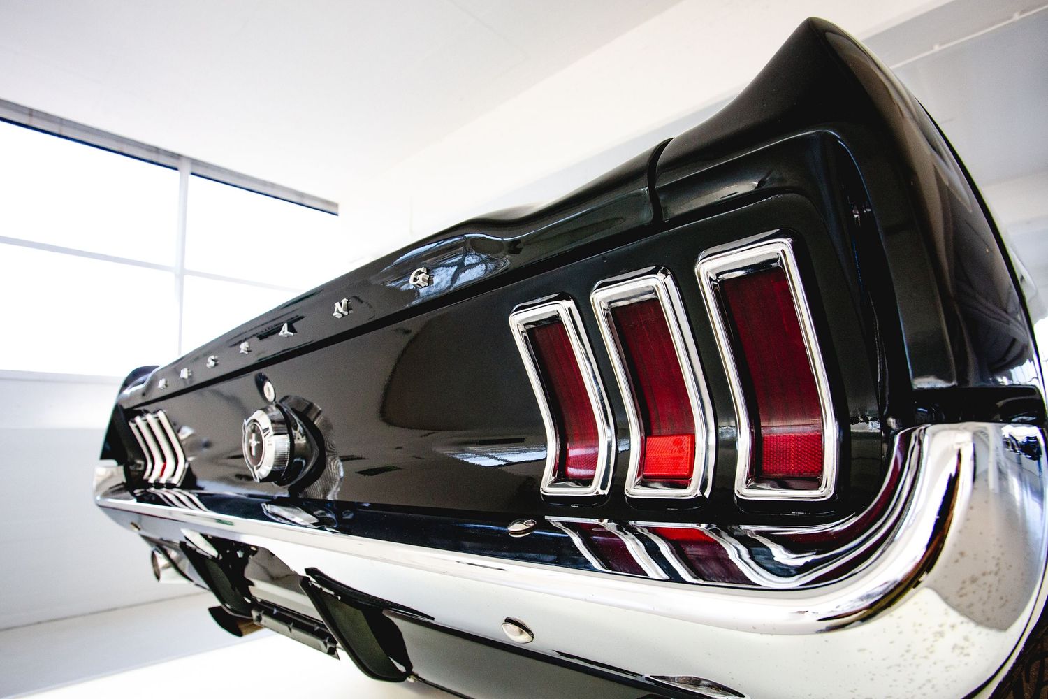Rear view of a classic black Ford Mustang GT with chrome tail lights in a showroom.