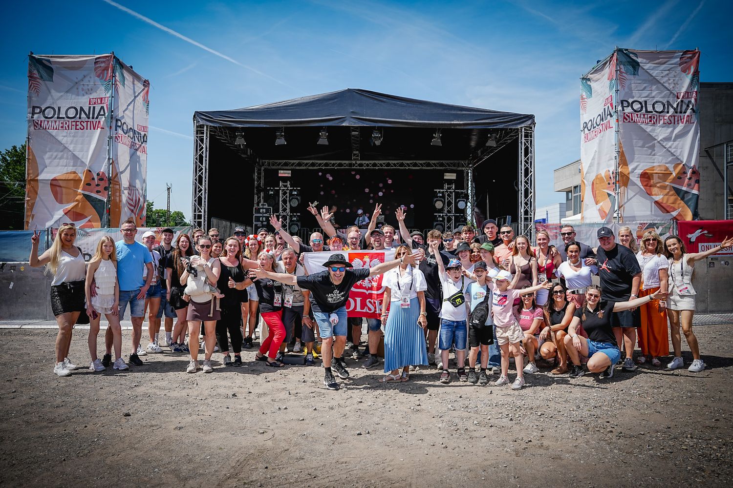 Large group poses together in front of Polonia Summer Festival main stage on a sunny day.