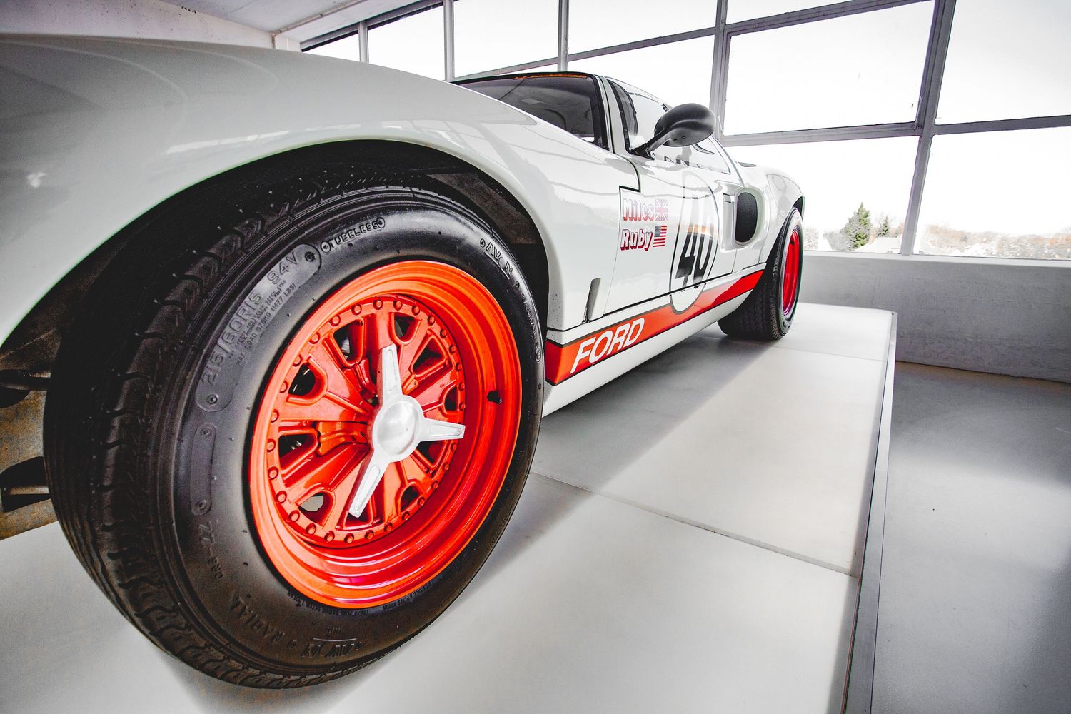 Close-up of a white racing car with bold red wheels and Ford GT40 livery displayed in a modern showroom.