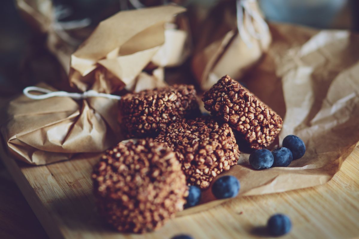 Homemade oat cookies and granola bars on parchment paper with fresh blueberries on a wooden cutting board.
