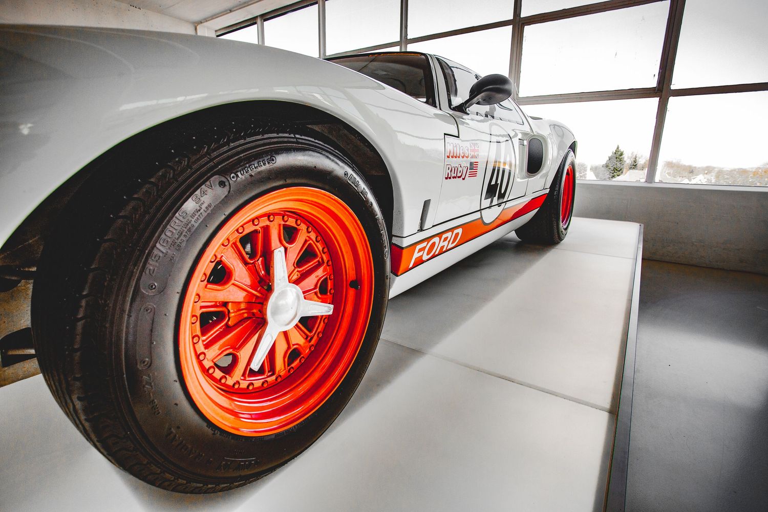 Vintage Ford GT40 race car with orange wheels displayed on a museum pedestal.