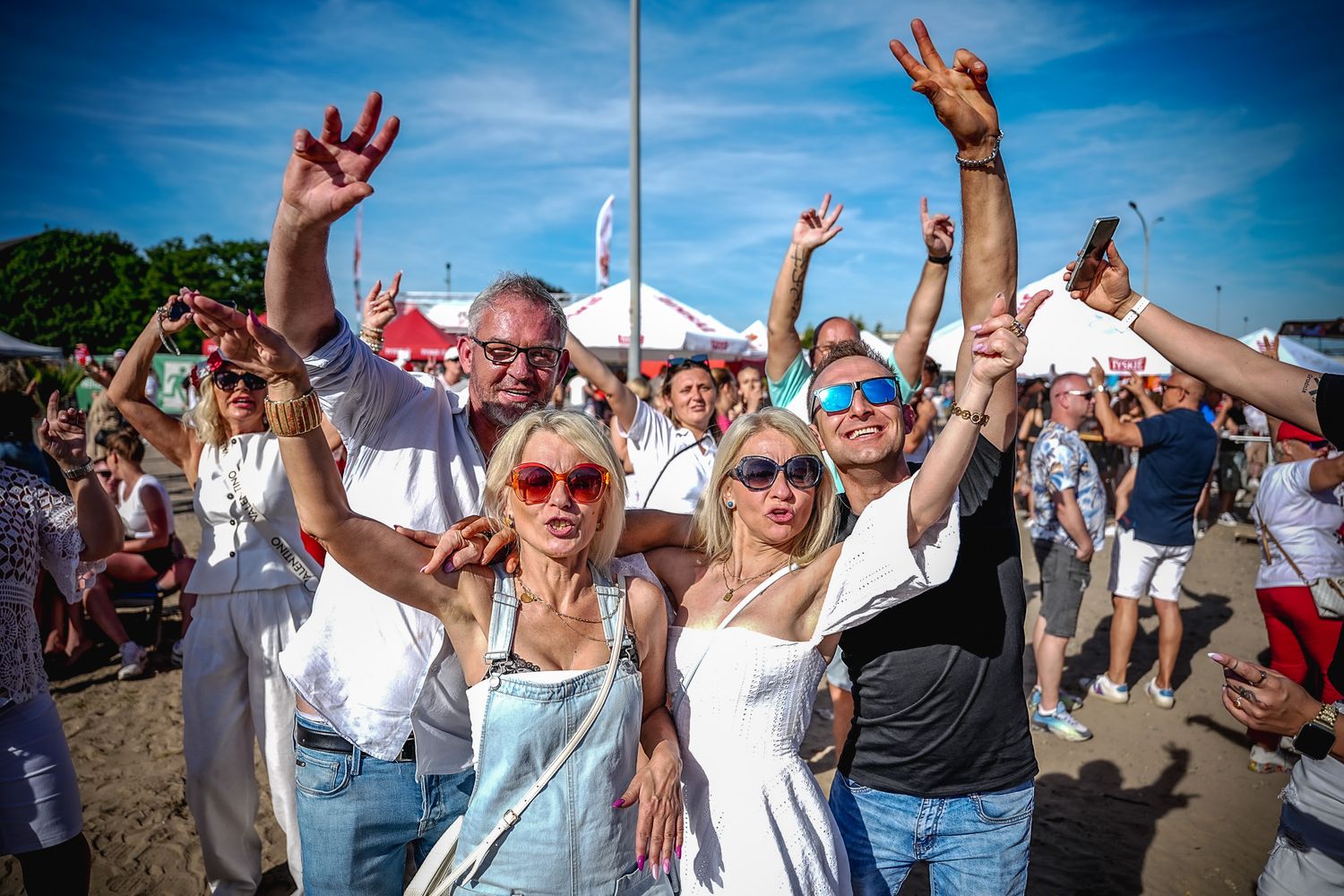 Crowd of happy people dancing and raising hands at an outdoor summer music festival on a sunny day.