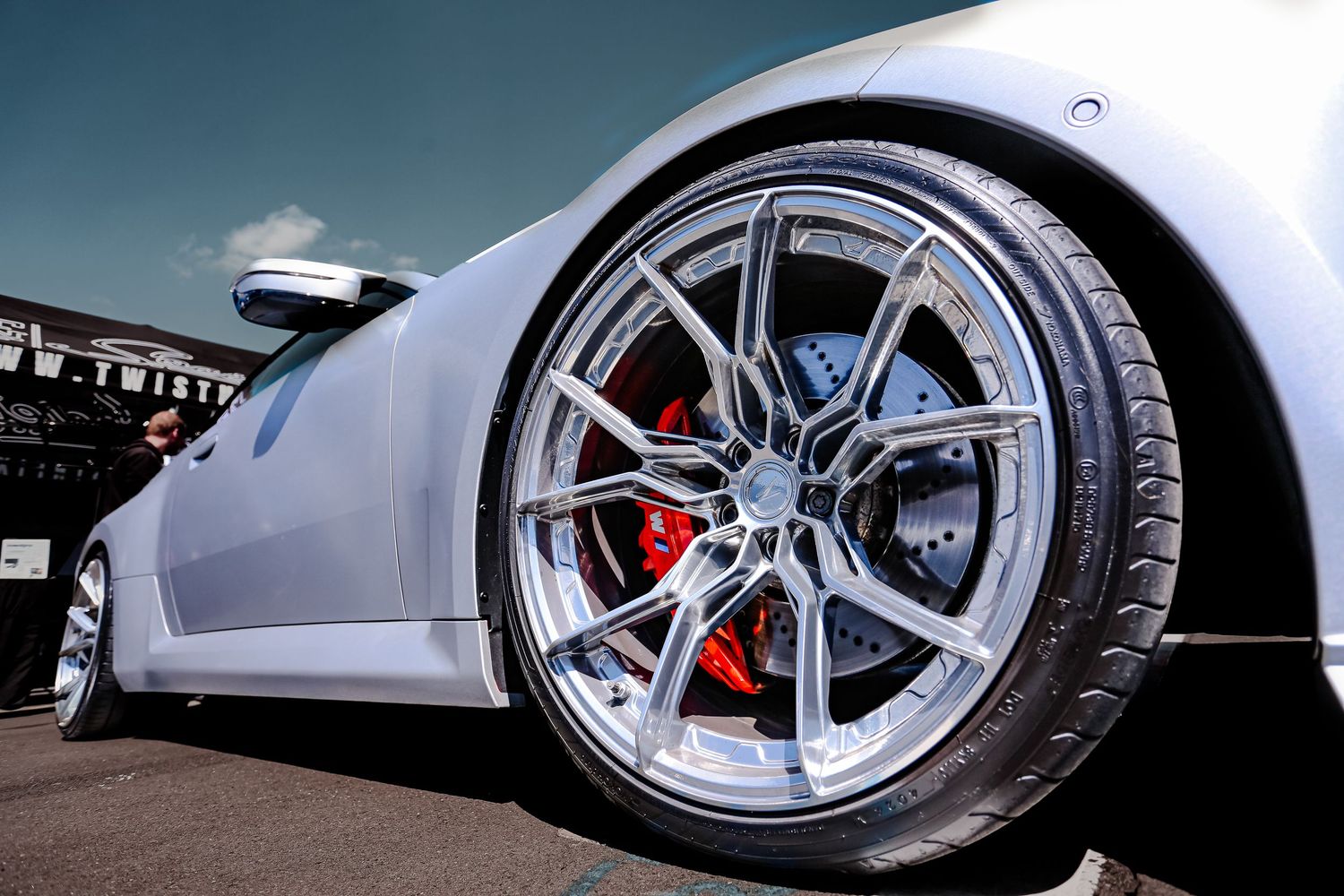 Low-angle close-up of a silver sports car featuring a multi-spoke alloy wheel with red brake calipers.