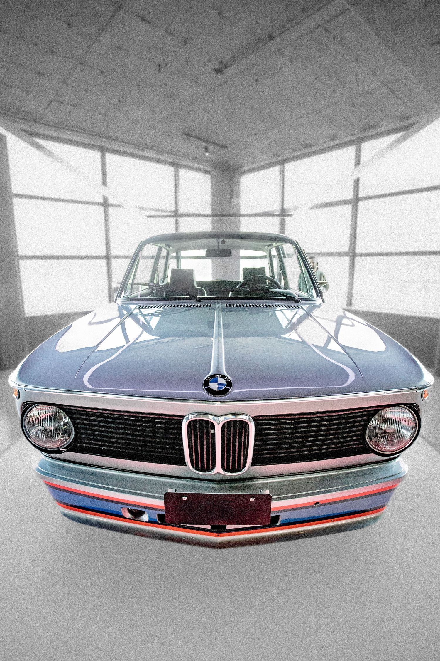 Vintage BMW 2002 with M stripes displayed in a modern showroom, front view.