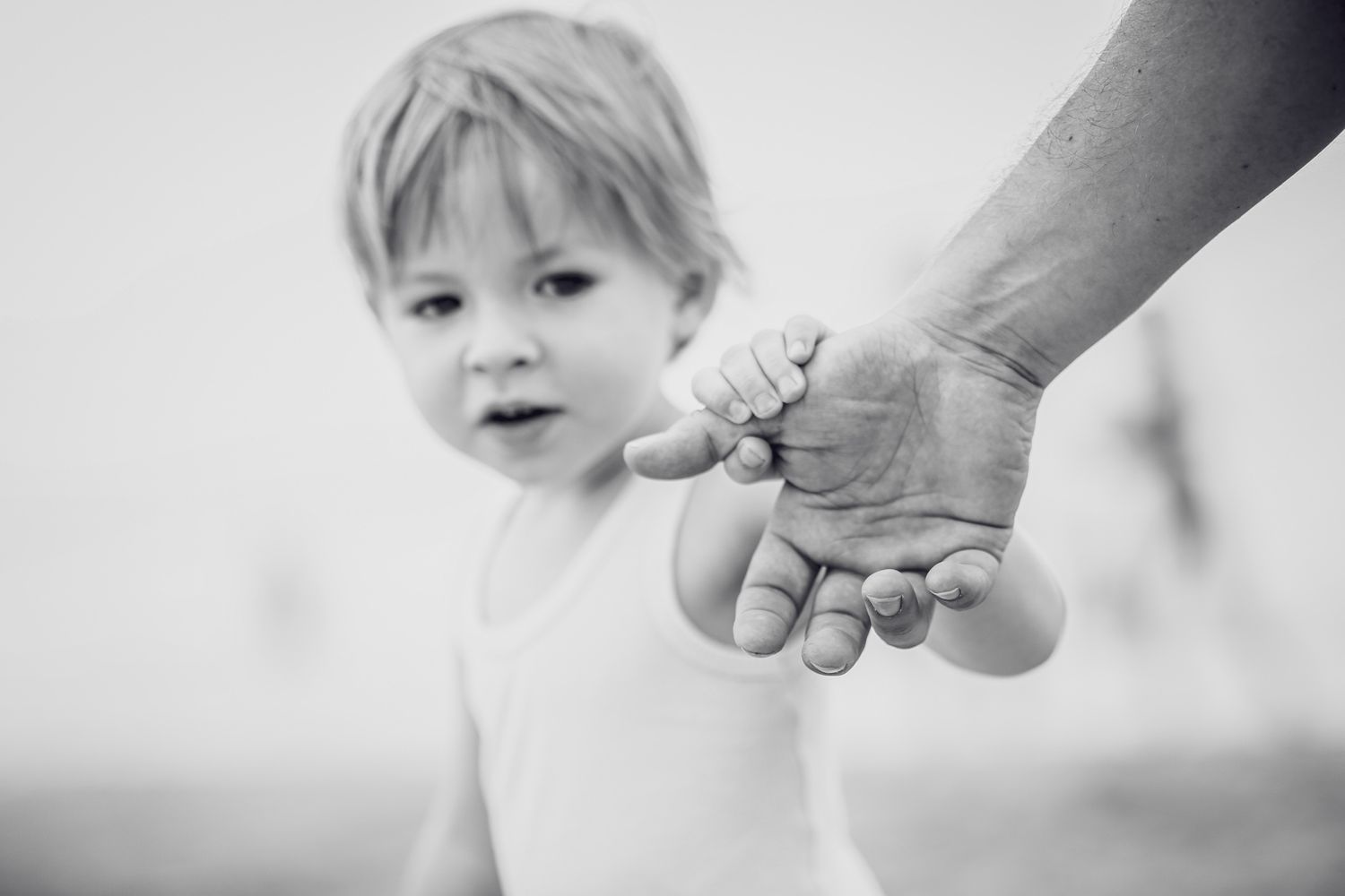 Black and white photo of a toddler holding an adult hand while walking outdoors.