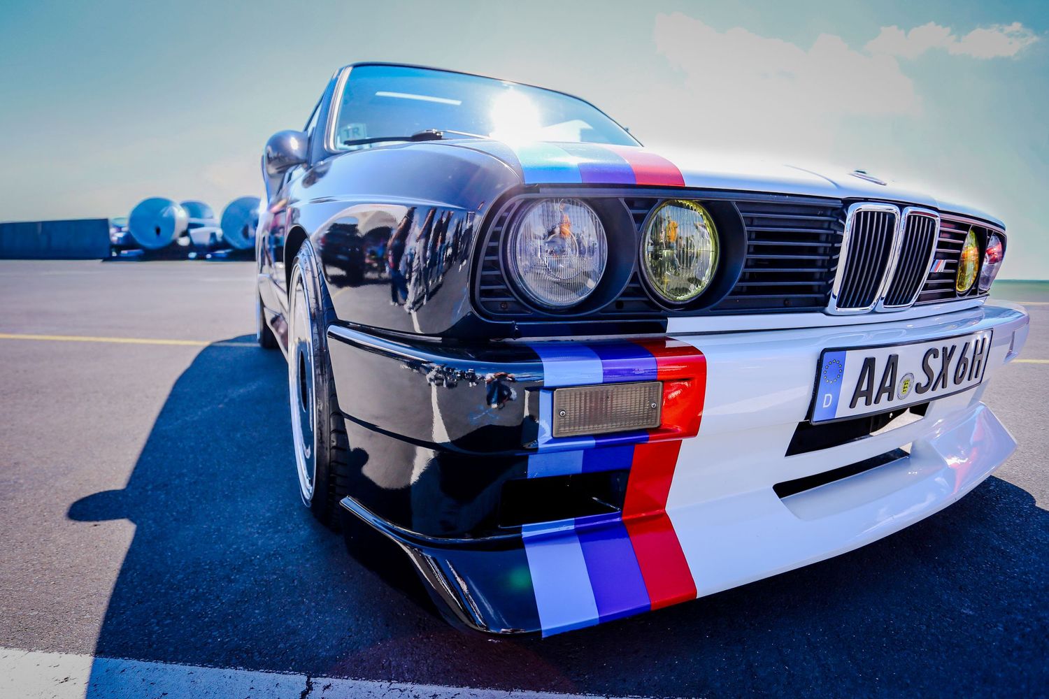 BMW E30 with M-colored bumper and racing livery parked on an airfield.
