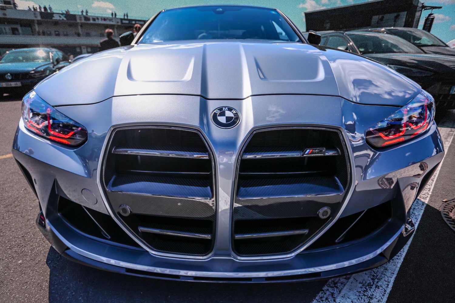 Front view of a silver BMW M4 with distinctive large kidney grilles and aggressive body styling at a car show.