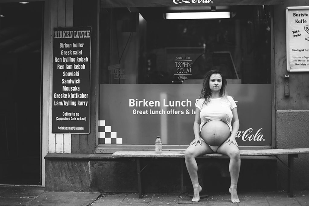 Black and white photo of a pregnant woman sitting outside a lunch restaurant on a bench.