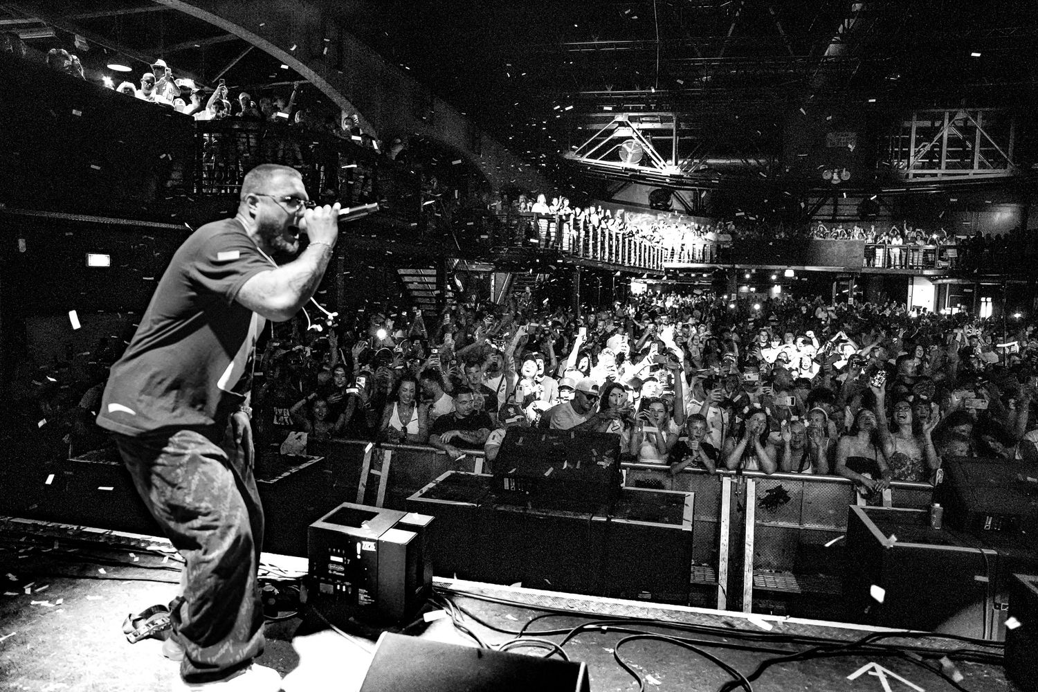 Black and white photo of a rapper performing on stage with microphone before a large Polonia music festival