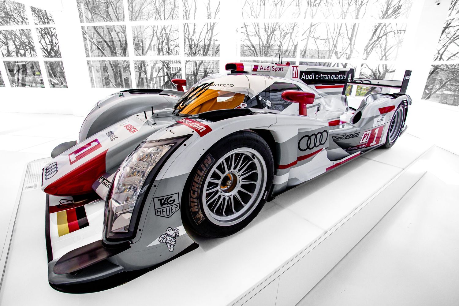 White Audi R18 e-tron quattro Le Mans prototype race car displayed in a museum.