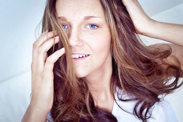 Beautiful woman with freckles and brown hair smiling softly against a white background.
