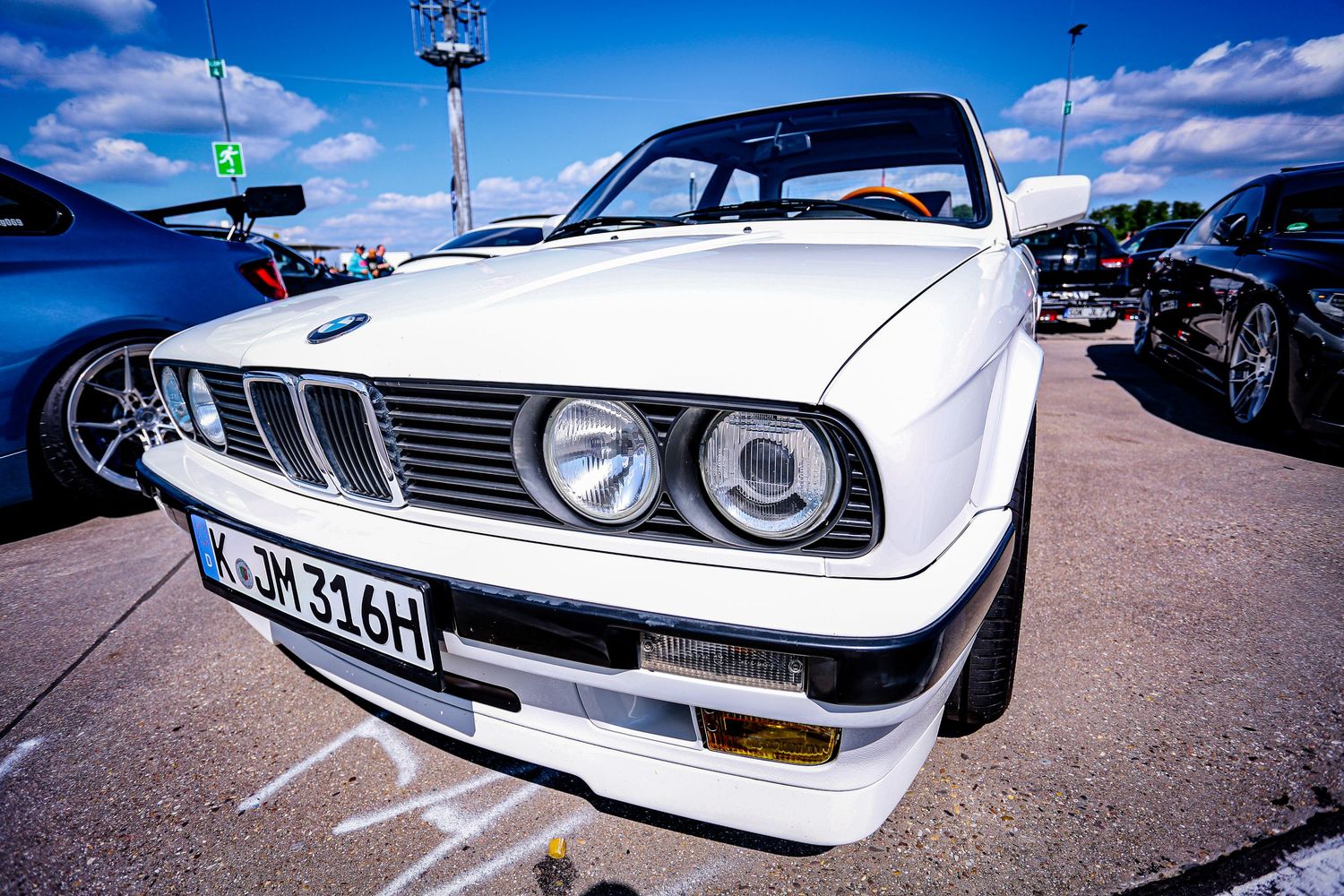 White BMW E30 3 Series with German license plate at an outdoor car show.
