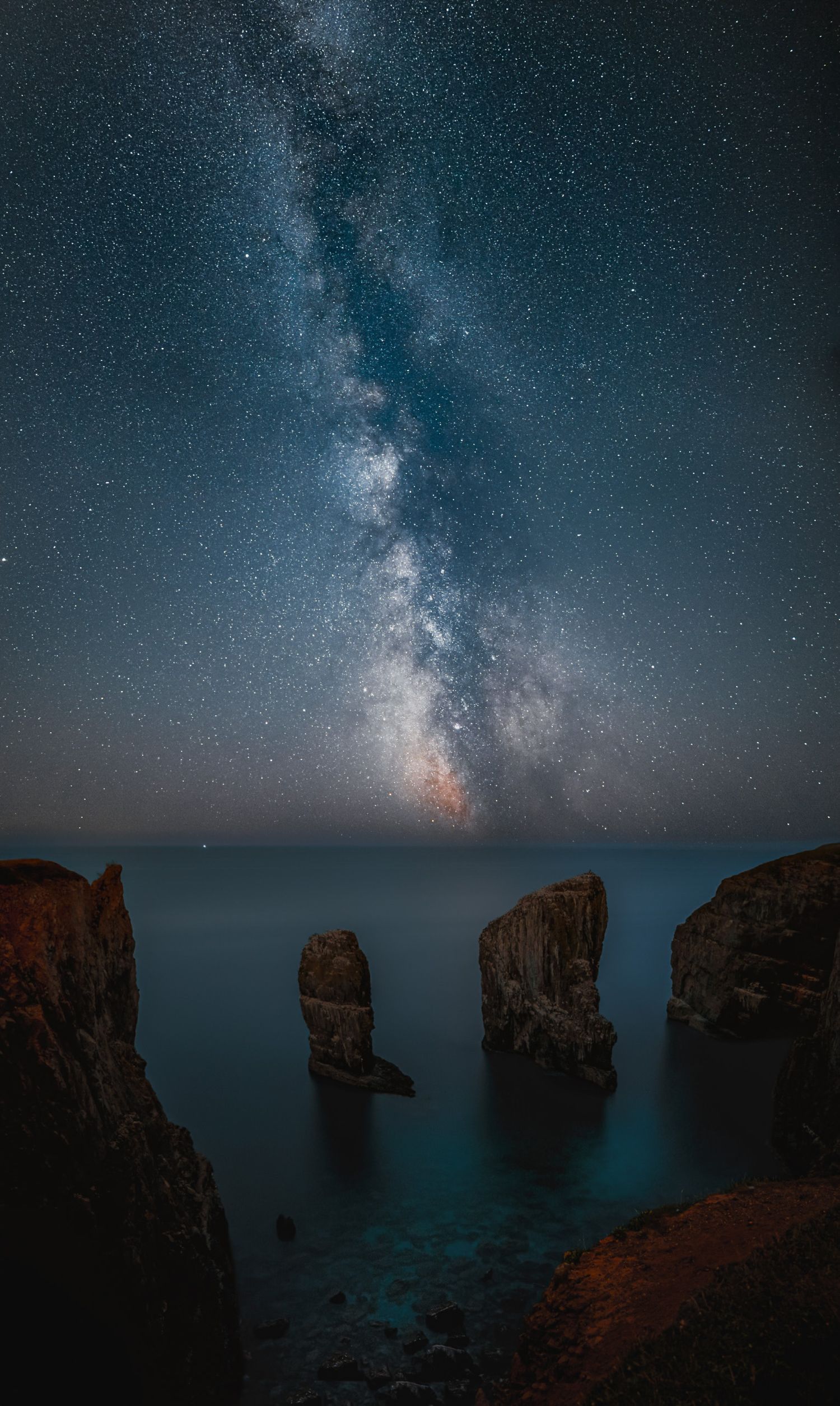 A vertical photo of the Milky Way galaxy stretching across a dark night sky over a silhouetted landscape