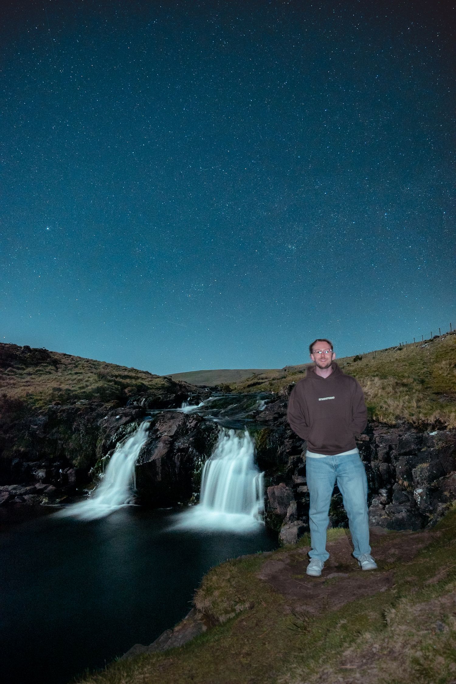 A person standing in front of a waterfall under a dark, starry sky.