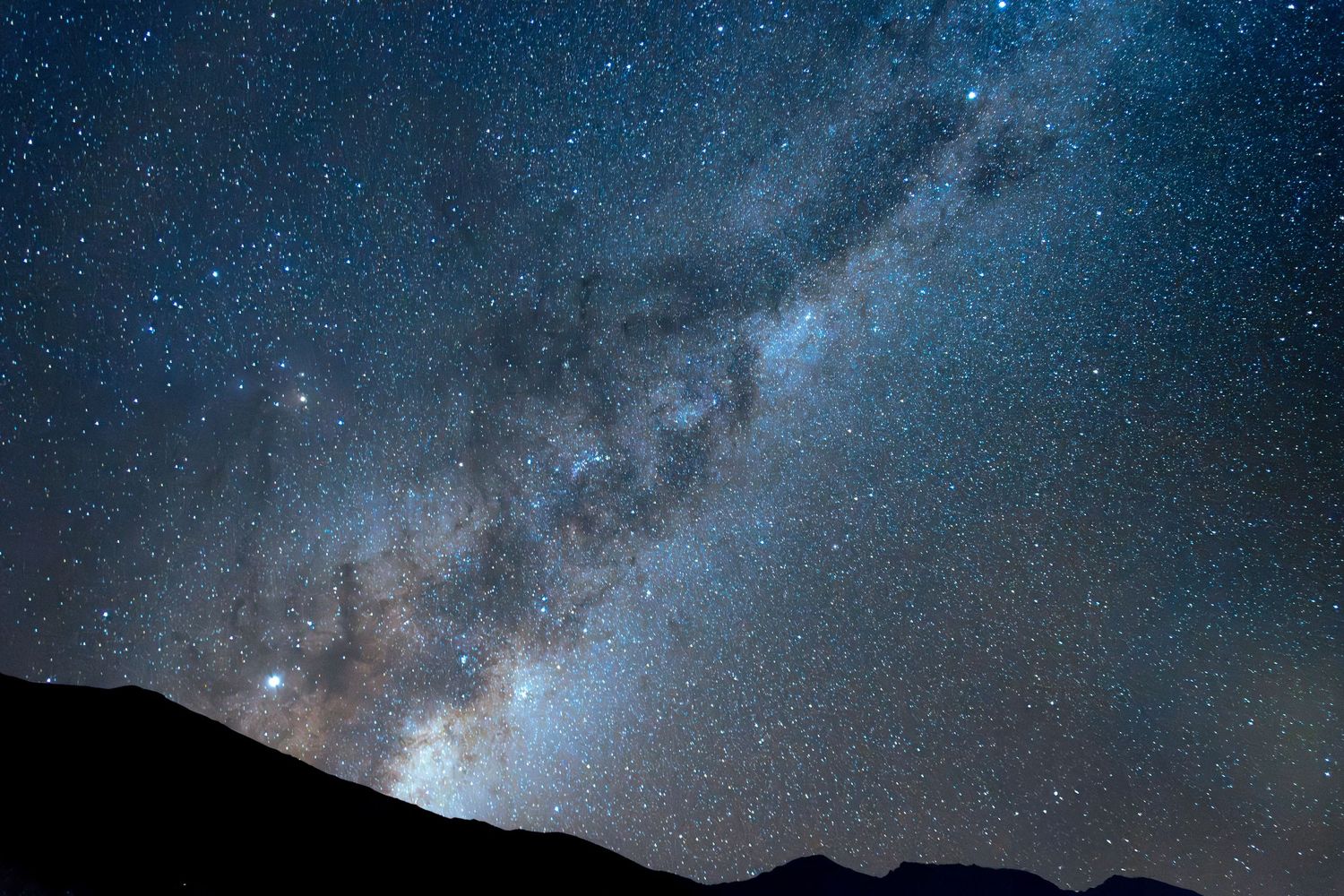 A starry night sky with the Milky Way clearly visible over a dark, silhouetted landscape.