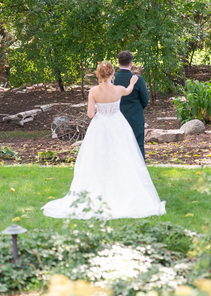 Bride in strapless white ball gown and groom in green suit share first look in lush garden.