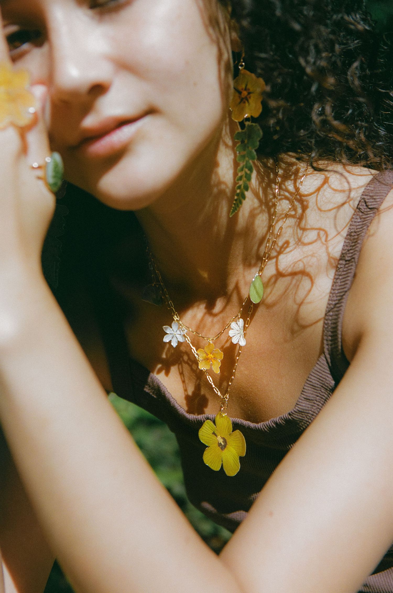 Close-up of woman wearing yellow flower necklace and earrings with green accents in sunlight.