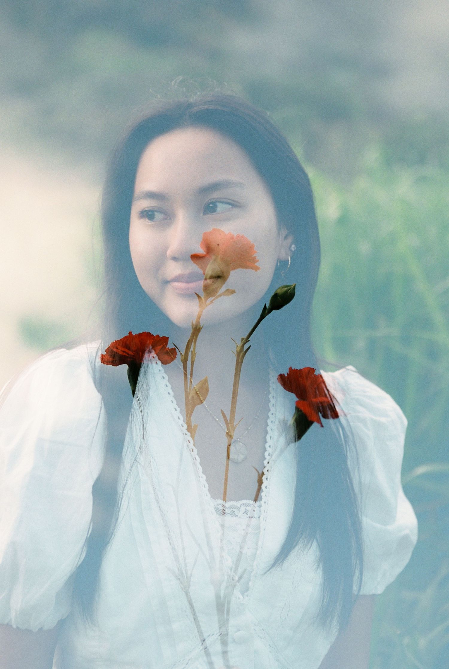 Dreamy double exposure portrait of a woman in white dress with red flowers in nature.