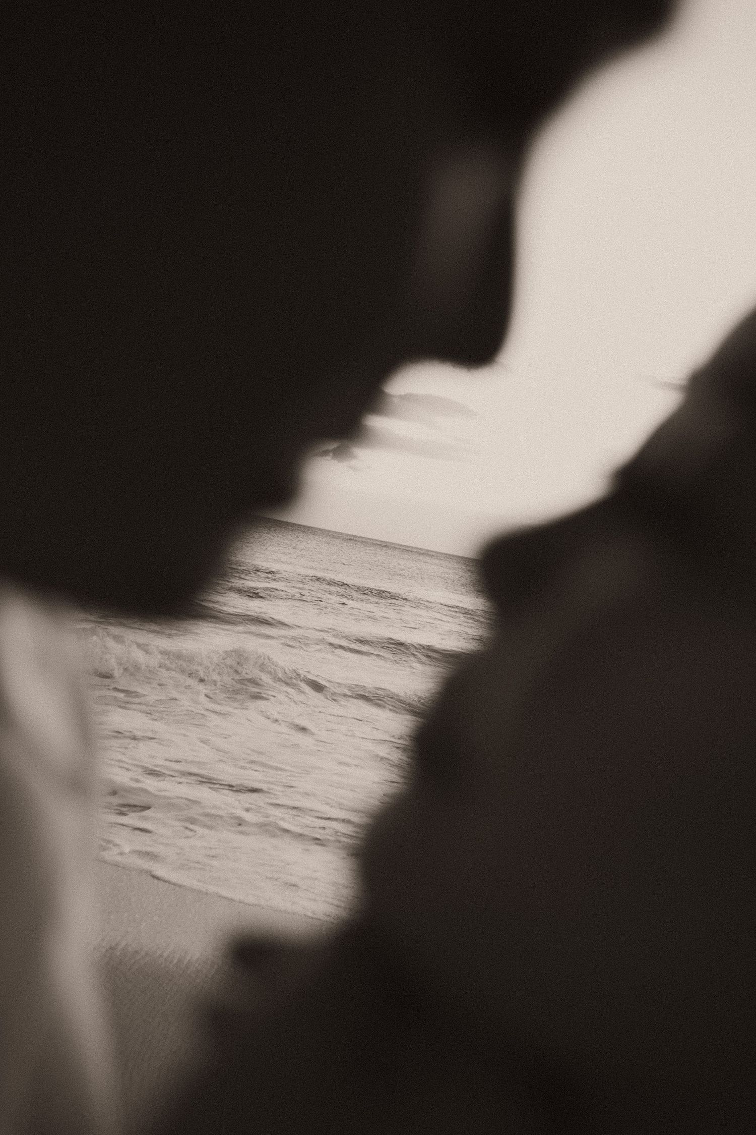Silhouetted couple about to kiss with ocean waves visible between them in sepia tone.