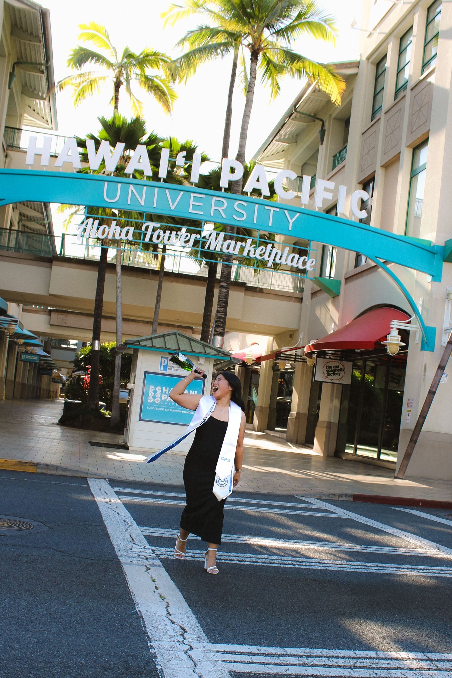 Graduate tosses cap under Hawaii Pacific University Aloha Tower Marketplace sign.