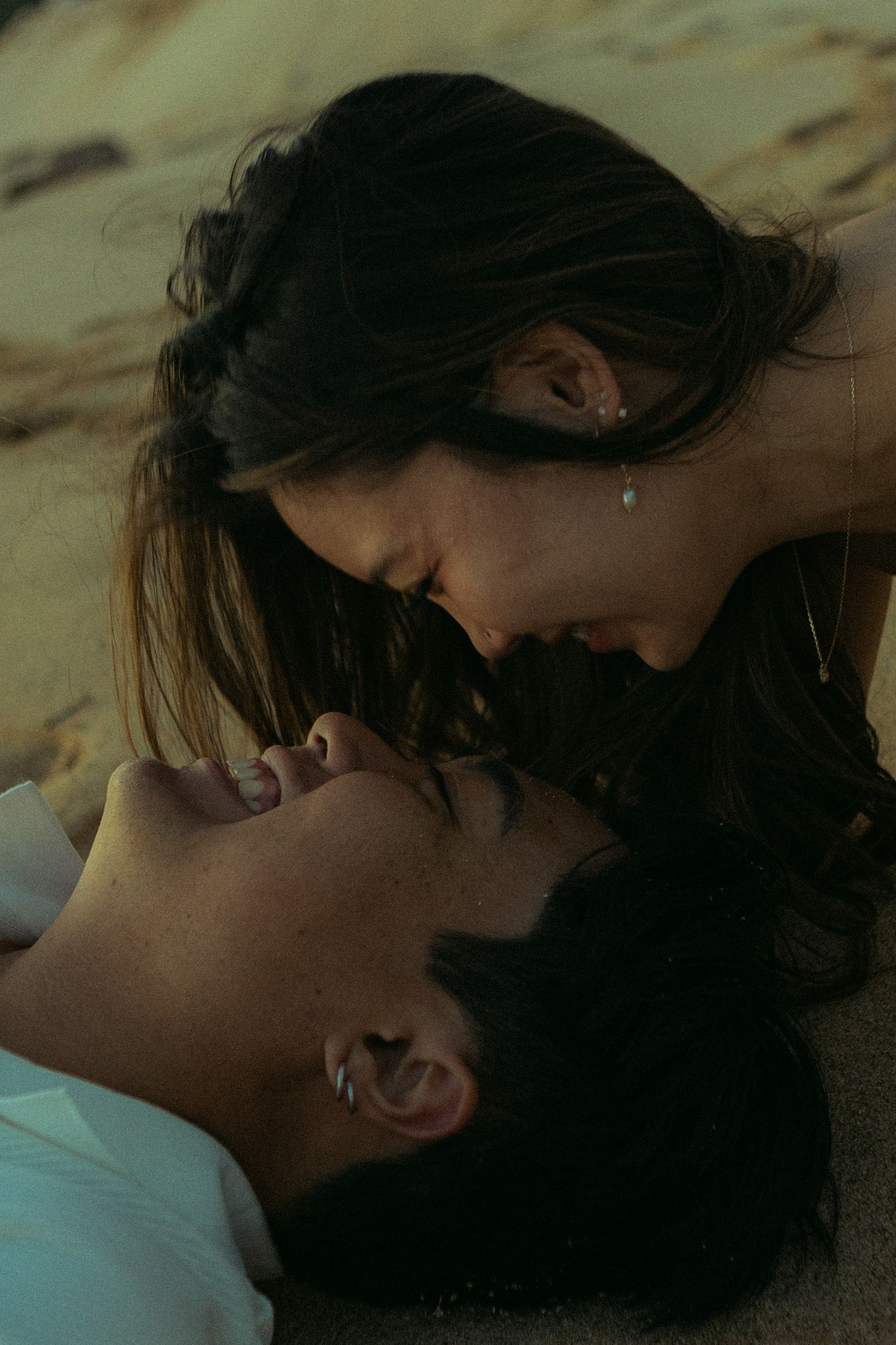 Intimate close-up of couple about to kiss while lying on sandy beach in dim light.