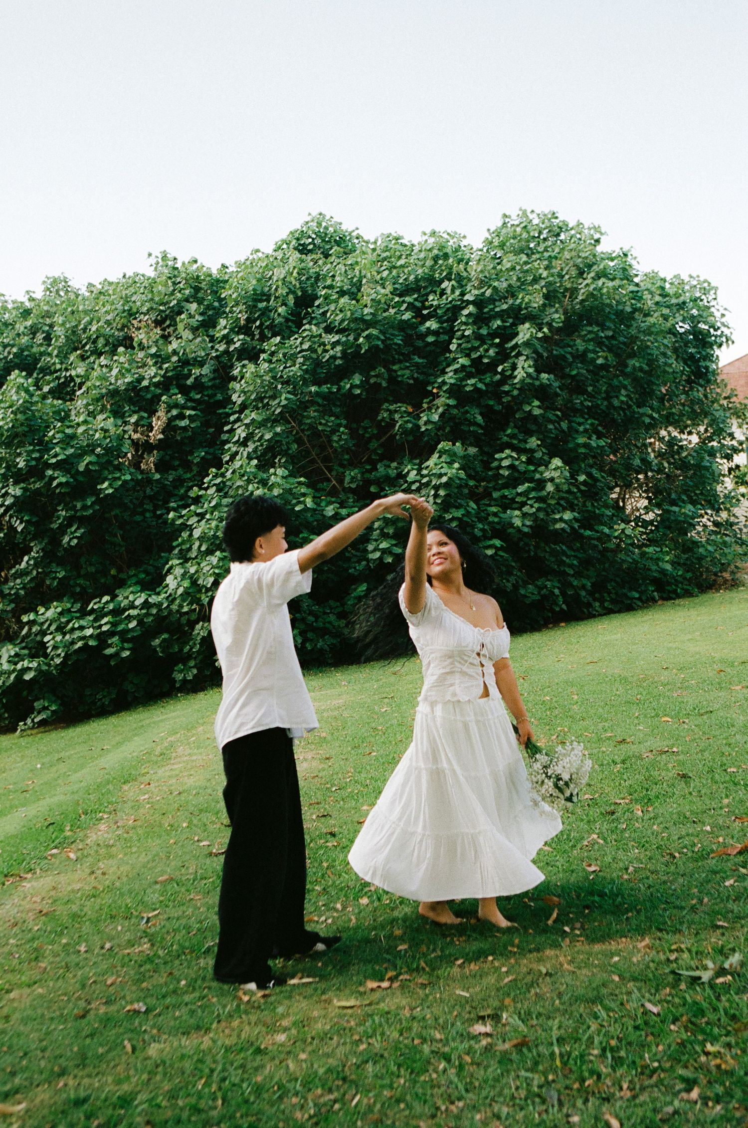 Couple dancing outdoors on green lawn with man spinning woman in white dress.