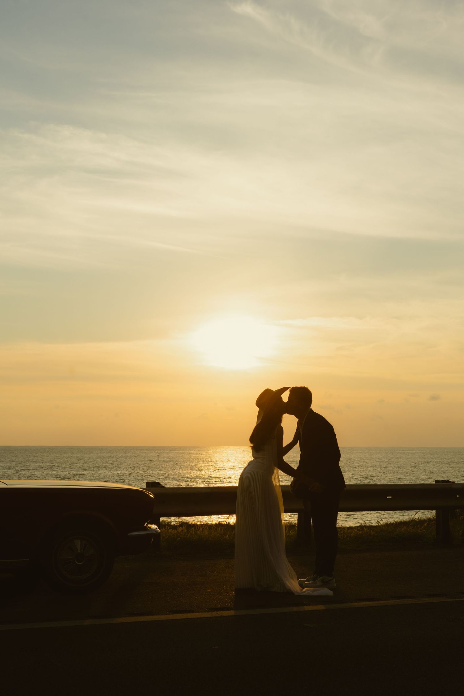 Silhouette of a couple kissing at sunset by the ocean, romantic golden sky backdrop.