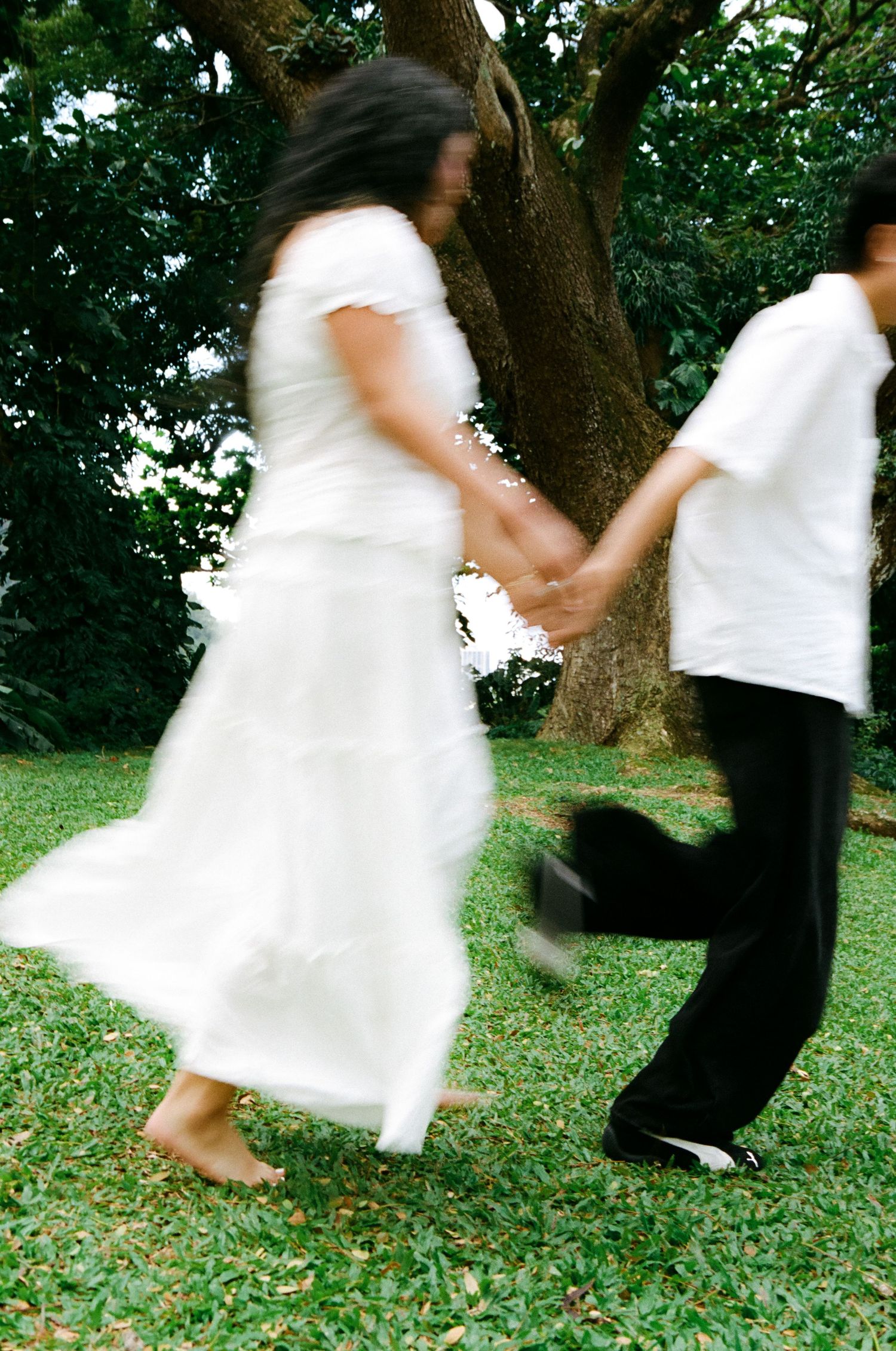 Couple holding hands and spinning together on green grass in a park.