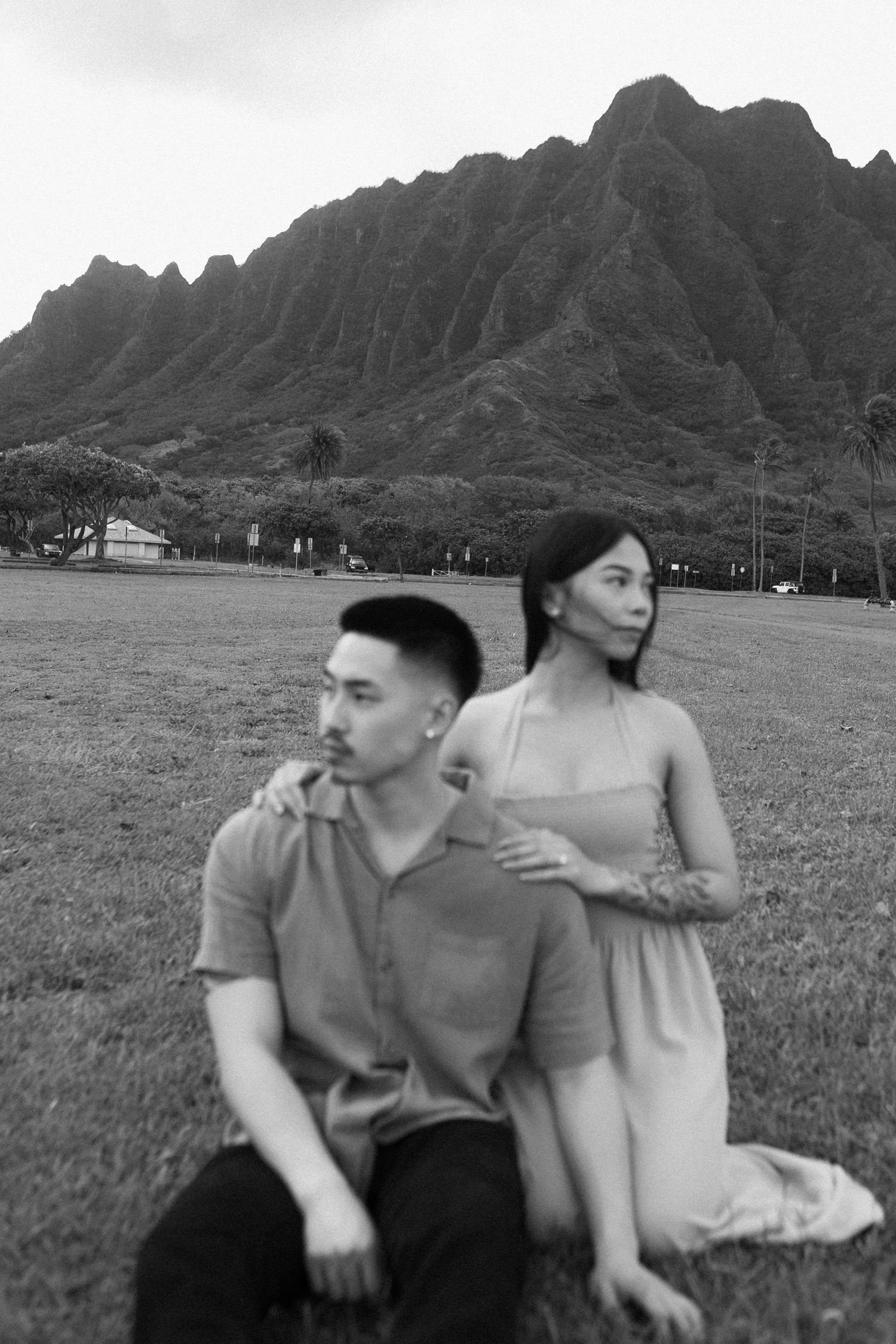 Black and white photo of Asian couple on grass with dramatic Ko'olau mountains behind them.
