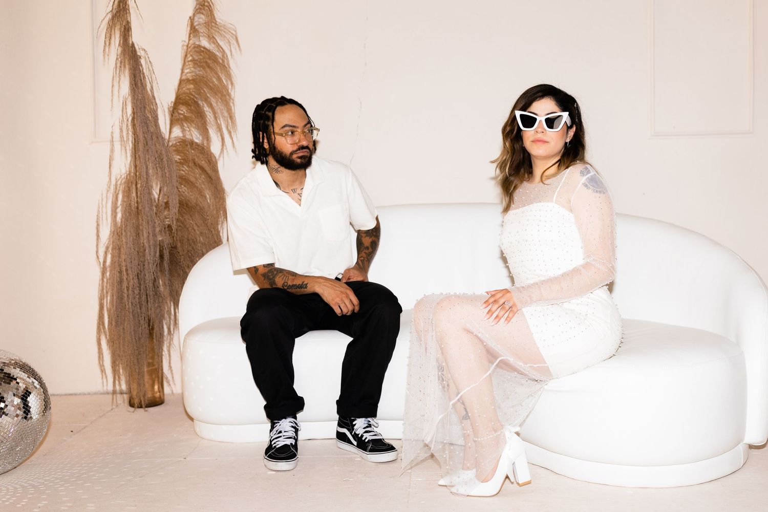 Stylish couple sitting on a white curved sofa in a modern minimalist studio.