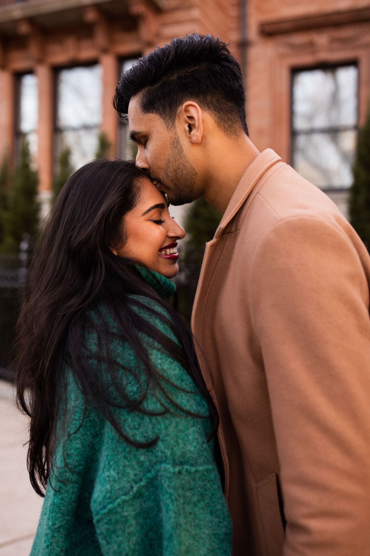 A romantic couple sharing a tender moment, the woman in a green coat smiling as the man leans in close outdoors.