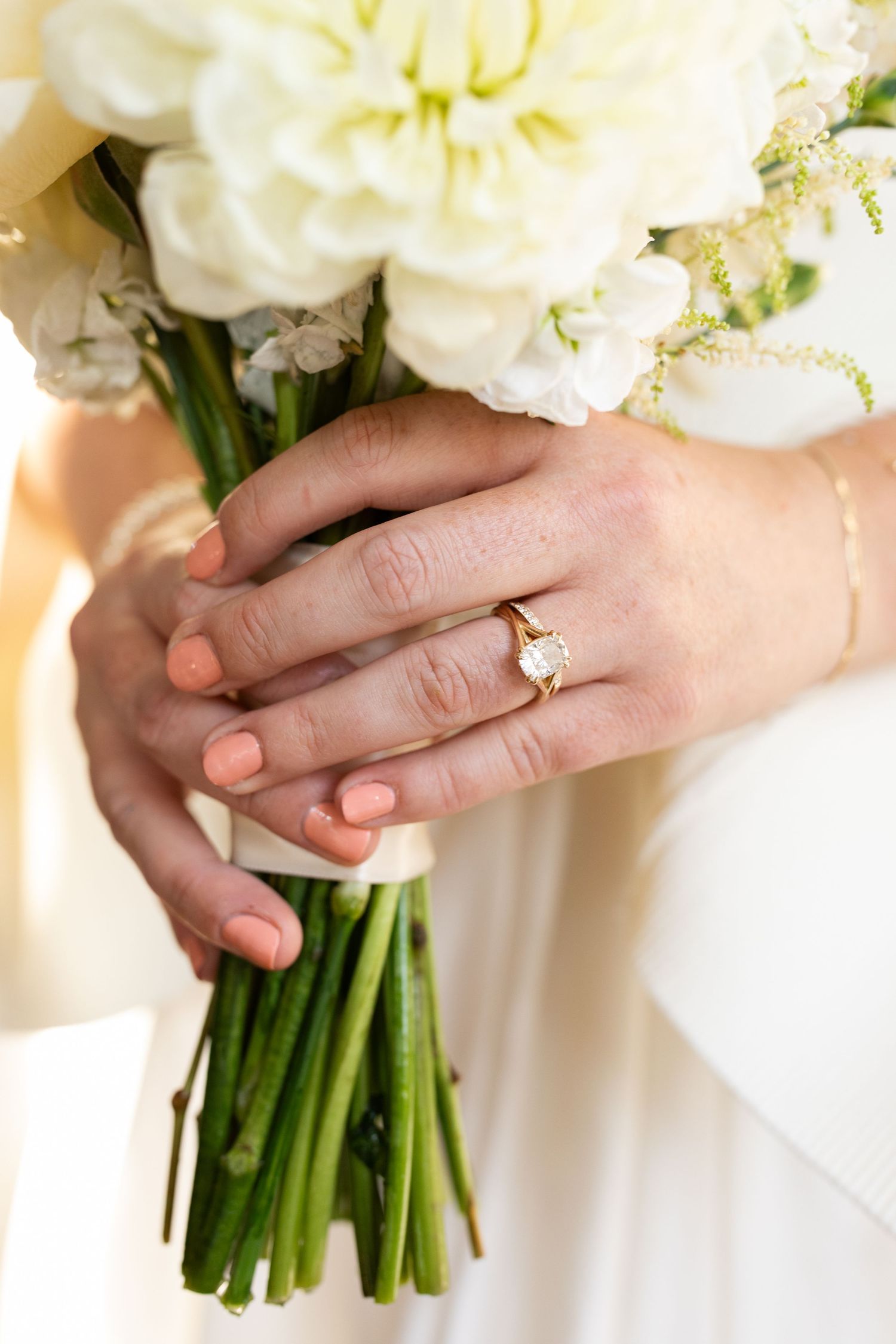 Close-up of bride's hands holding white floral bouquet with gold diamond engagement ring.