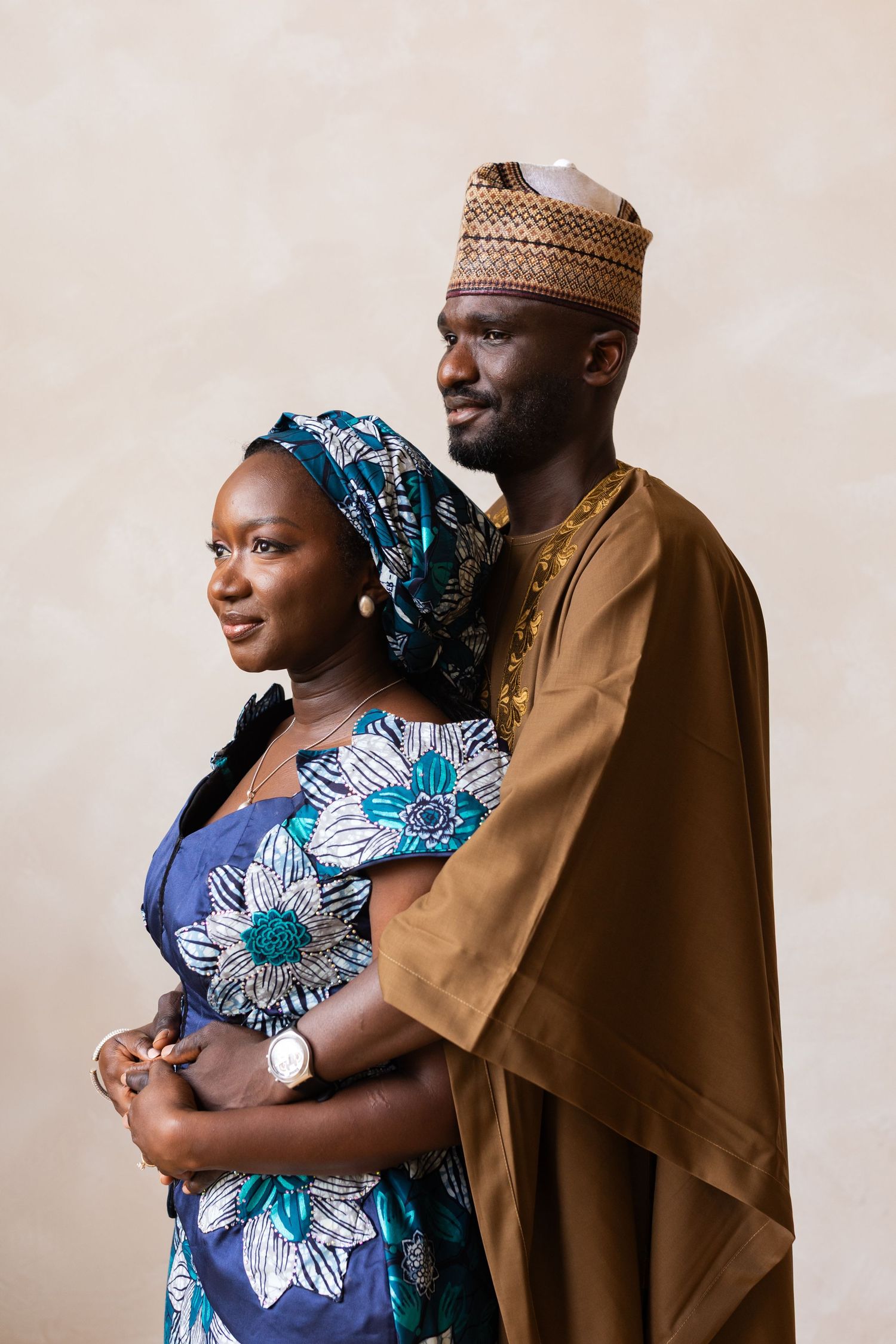 Couple in traditional attire embracing warmly, man in brown agbada and woman in blue dress.