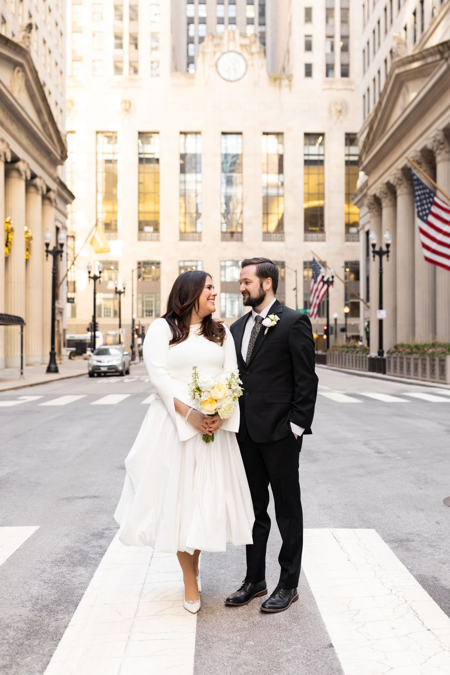 Bride and groom exchange glances on a crosswalk with Chicago Board of Trade building in background.