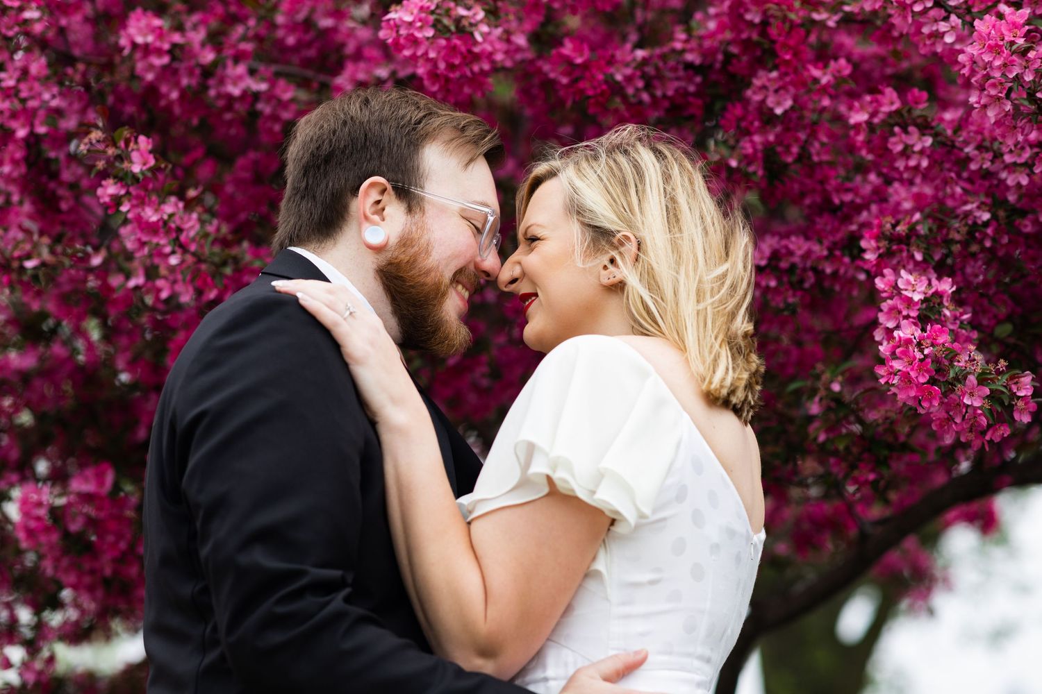 Happy couple sharing an intimate moment in front of vibrant pink cherry blossoms.