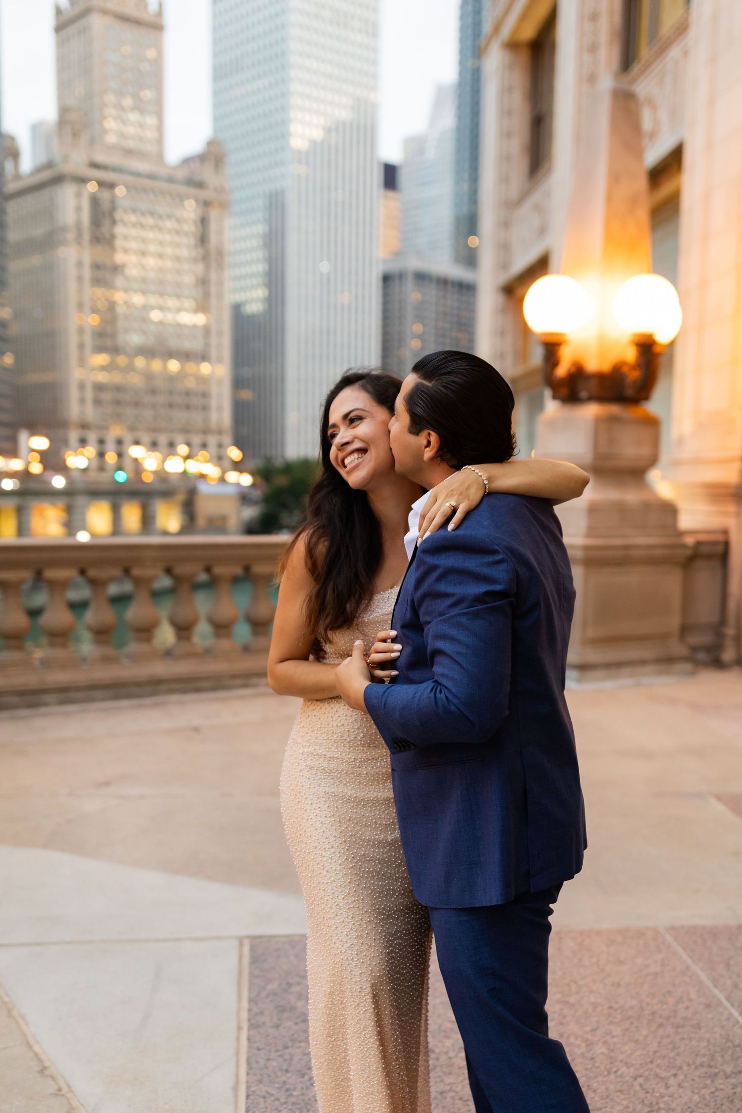 Romantic couple embracing near ornate lamp post on Chicago Riverwalk with glowing city skyline.