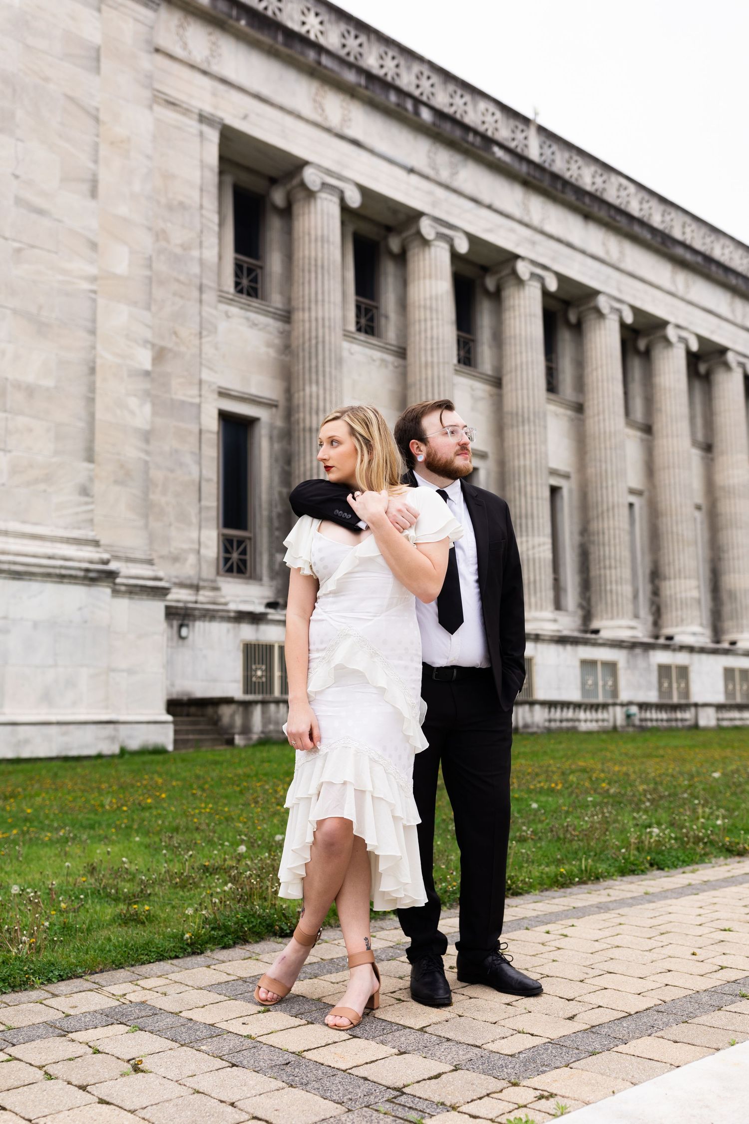 Elegant couple poses together outside a grand neoclassical stone building with tall columns.