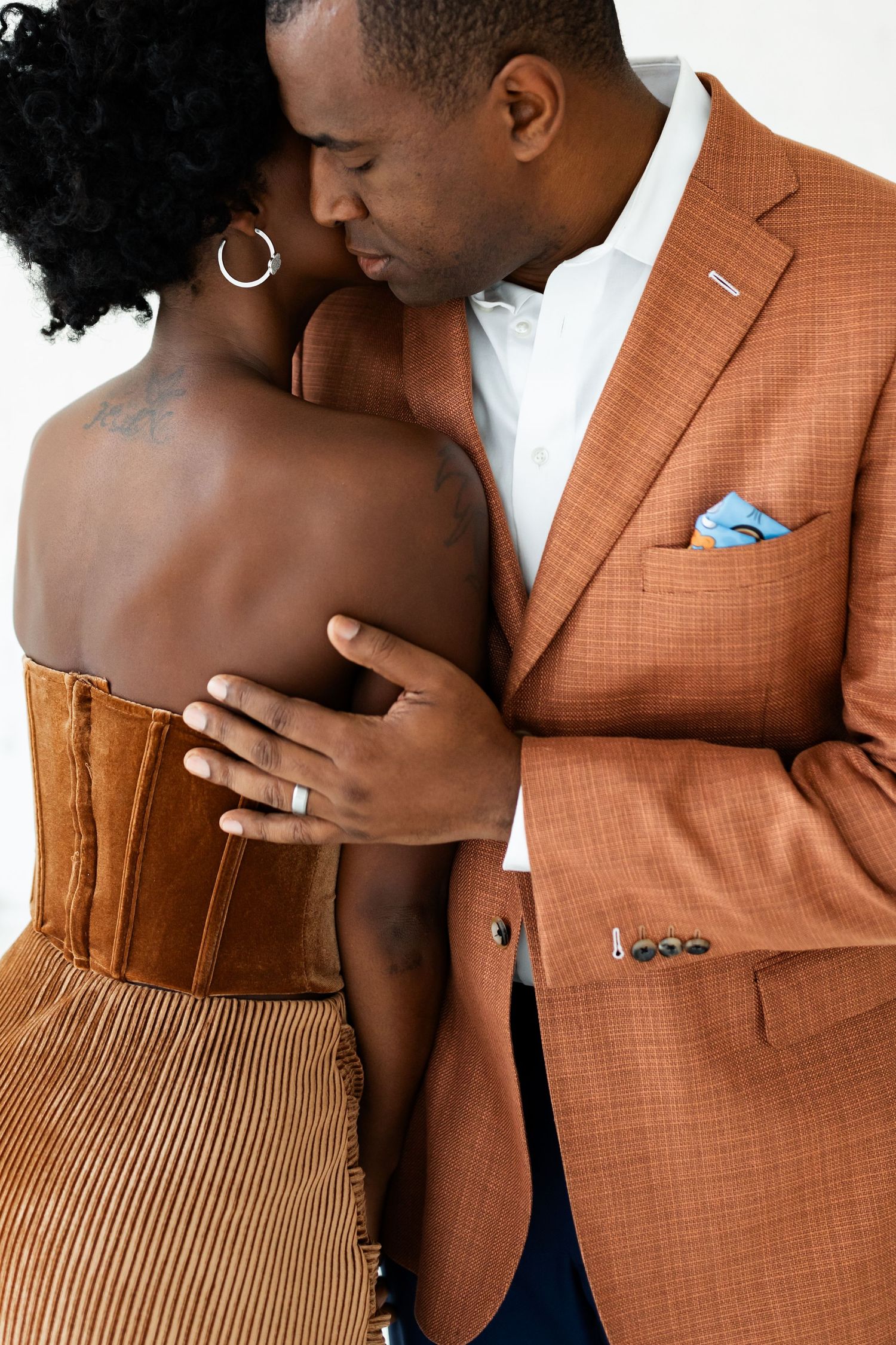 An intimate moment as a well-dressed couple shares a kiss, the man in an orange blazer embracing her.
