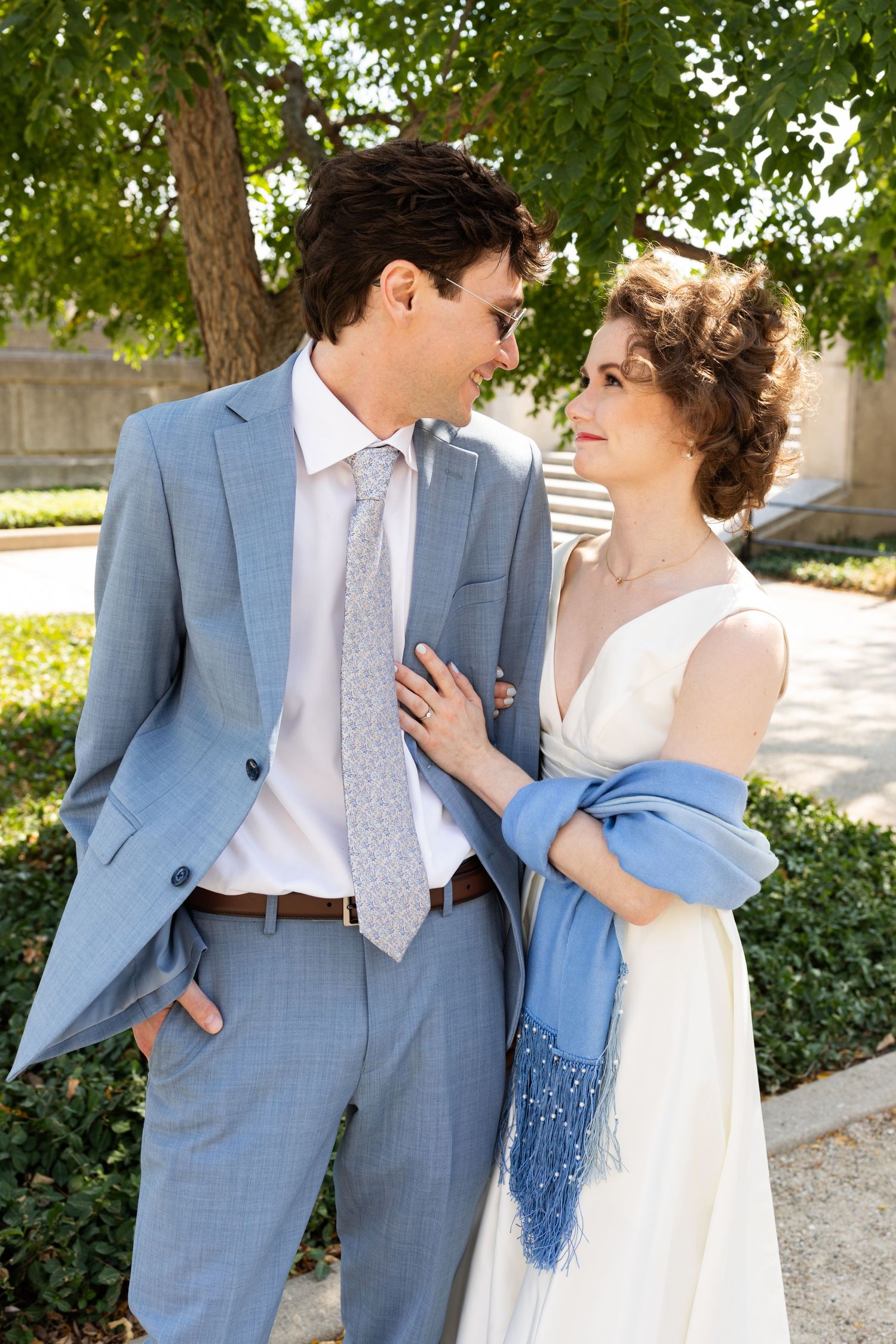 Bride and groom gazing at each other outdoors, groom in blue suit, bride with blue shawl.