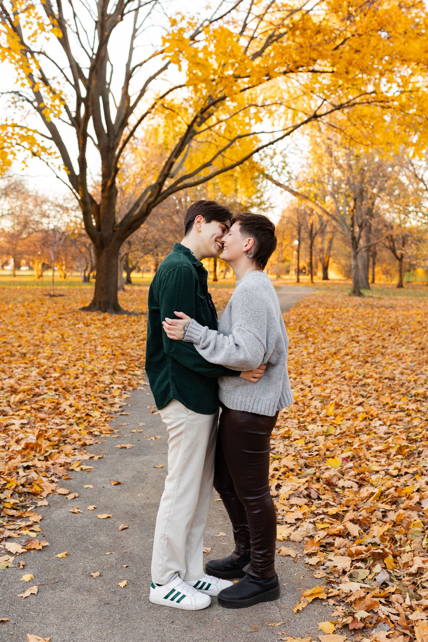 Couple about to kiss on a park path surrounded by vibrant yellow autumn foliage and fallen leaves.