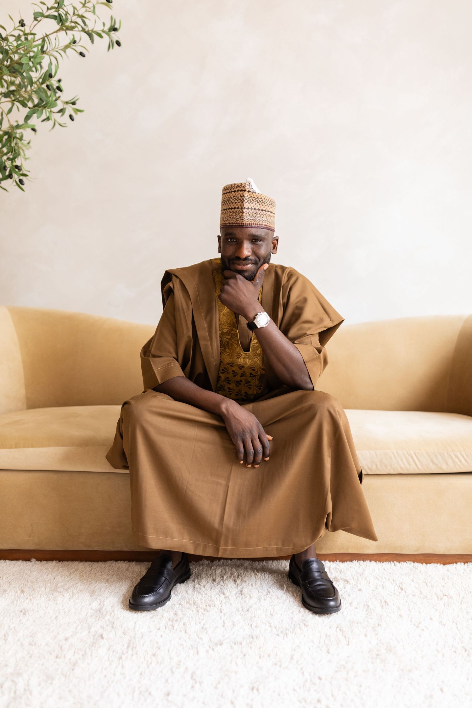 Man in brown traditional outfit seated confidently on a sofa.