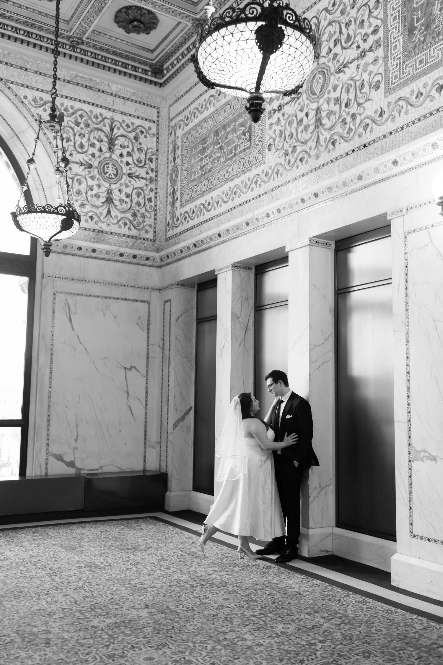 Bride and groom sharing a romantic moment in a grand ornate marble hall with intricate ceiling details.
