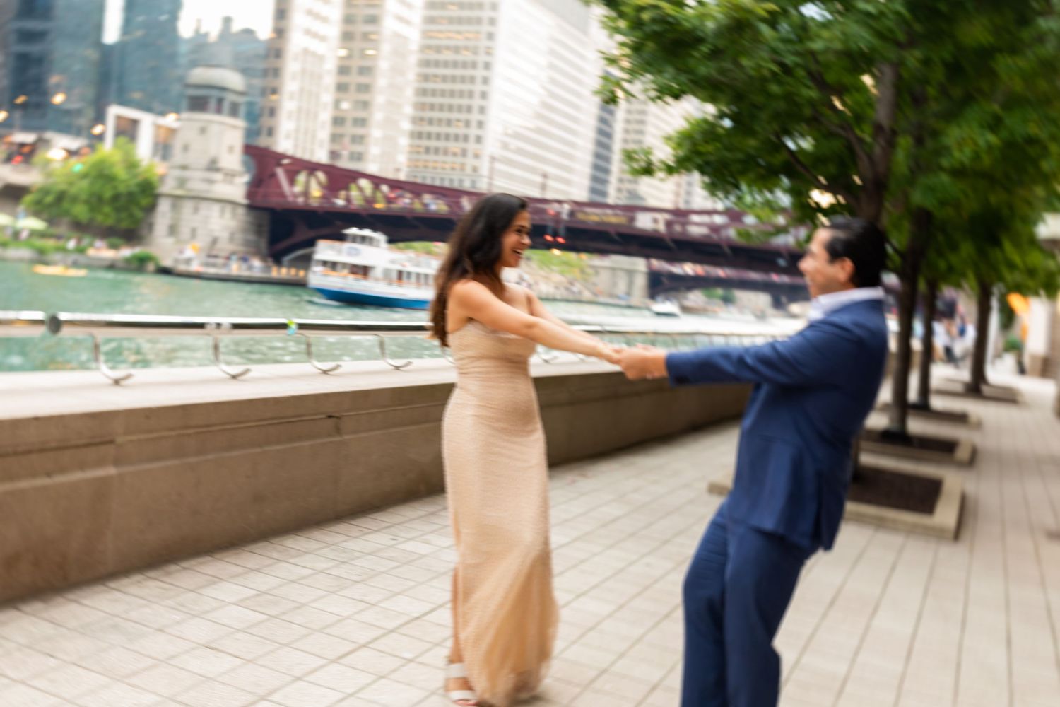 Bride in gold sequin gown holding grooms hand along Chicago Riverwalk with bridge in background.